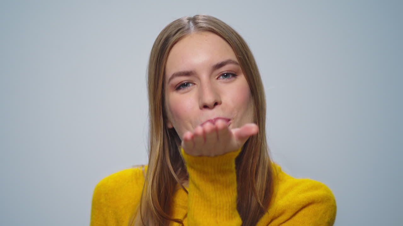 retrato de una mujer positiva enviando un beso en el aire a la cámara sobre un fondo gris.