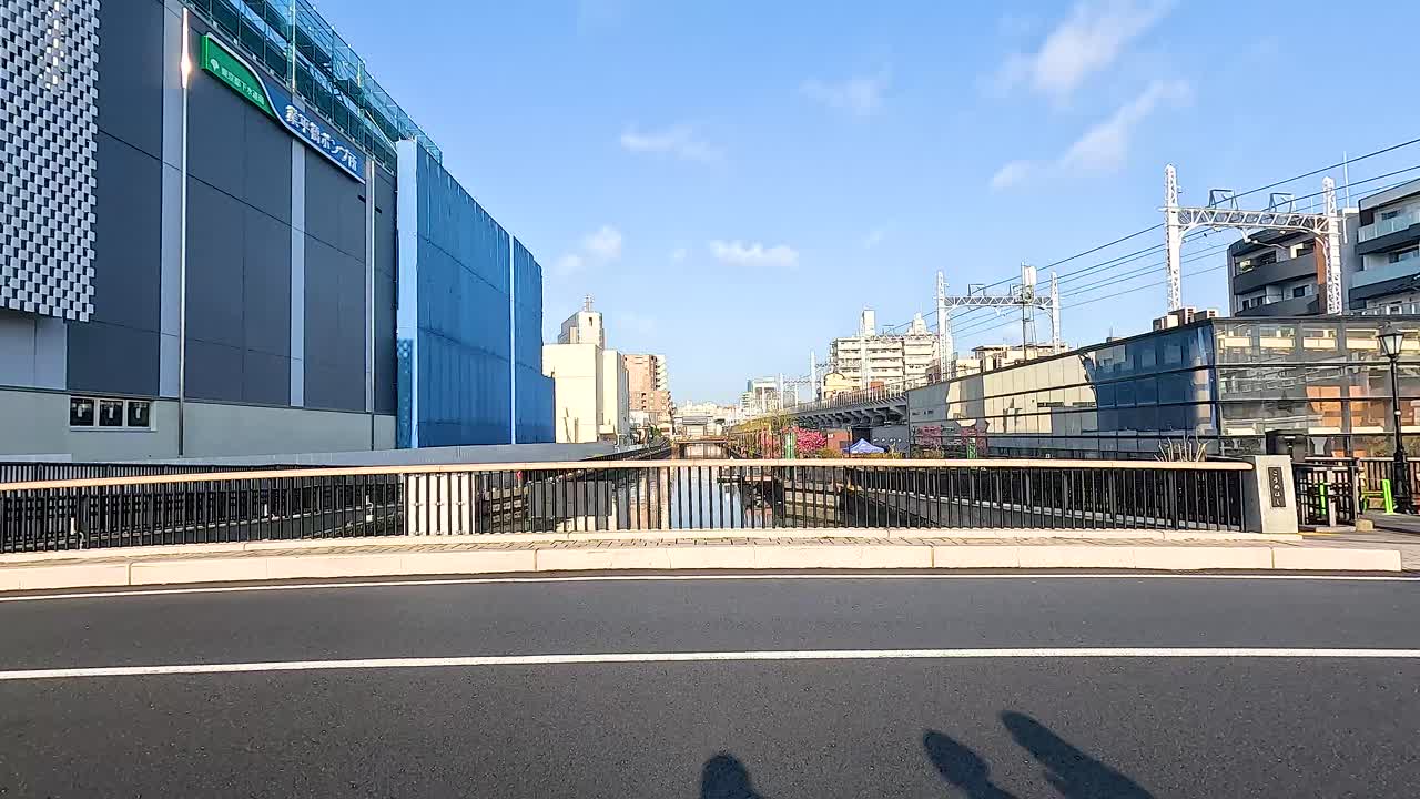 Shadows cast on a Tokyo street as vehicles pass by, under clear skies and bright sunlight, creating dynamic urban movement