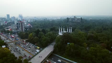 Aerial-view-dolly-in-on-a-foggy-day-of-the-Shiro-Bridge-and-the-Altar-a-la-Patria-monument-in-Chapultepec-Forest,-Chapultepec-Castle-diffused-in-the-mist,-Mexico-City