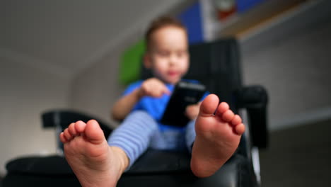 toddler's bare feet close up. low angle view on the baby boy with smartphone in hands. blurred backdrop.