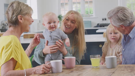 grandparents with adult daughter and grandchildren sitting around kitchen table at home