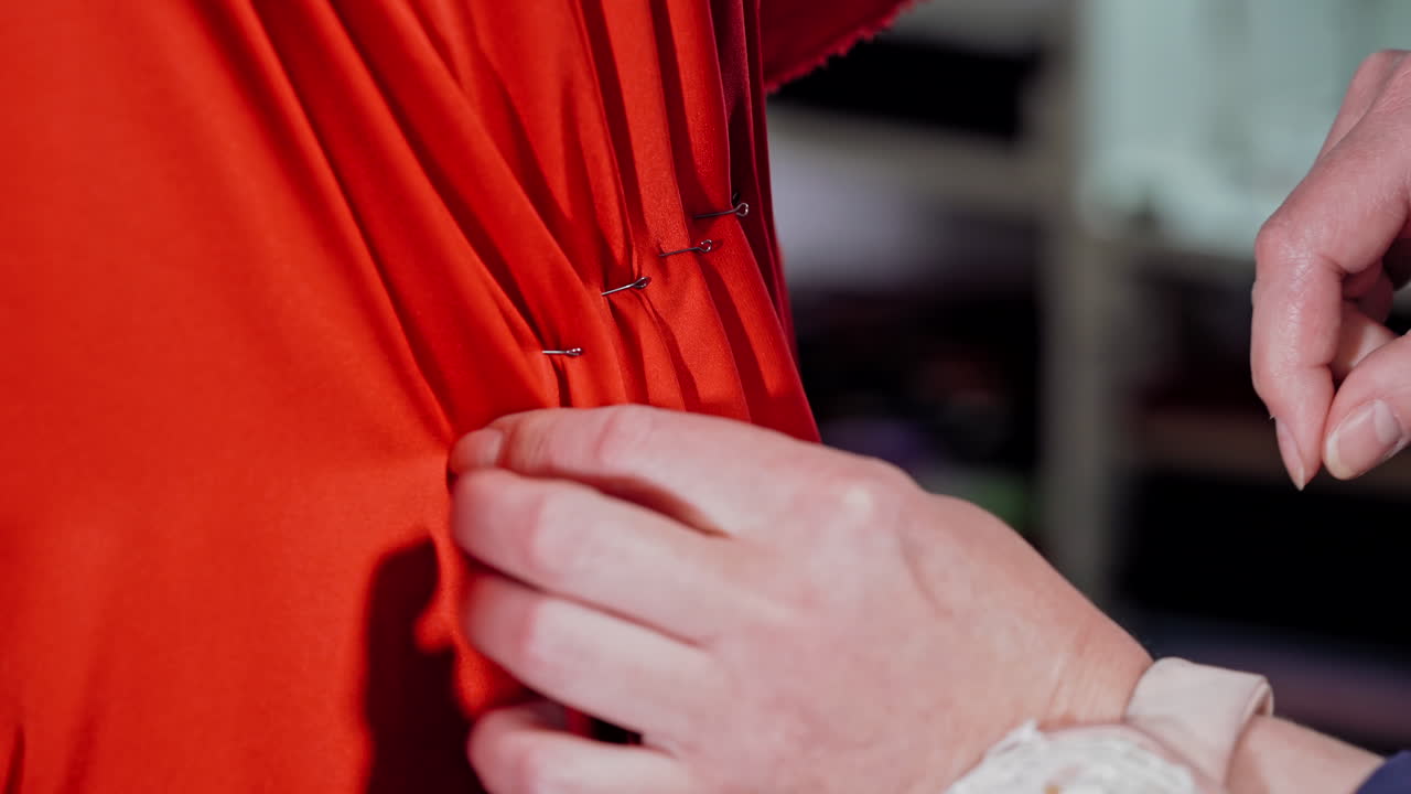Hands of a professional tailor working with red cloth on mannequin with pins. Seamstress pinning on red fabric on the dummy to sew a nice dress. Close-up.