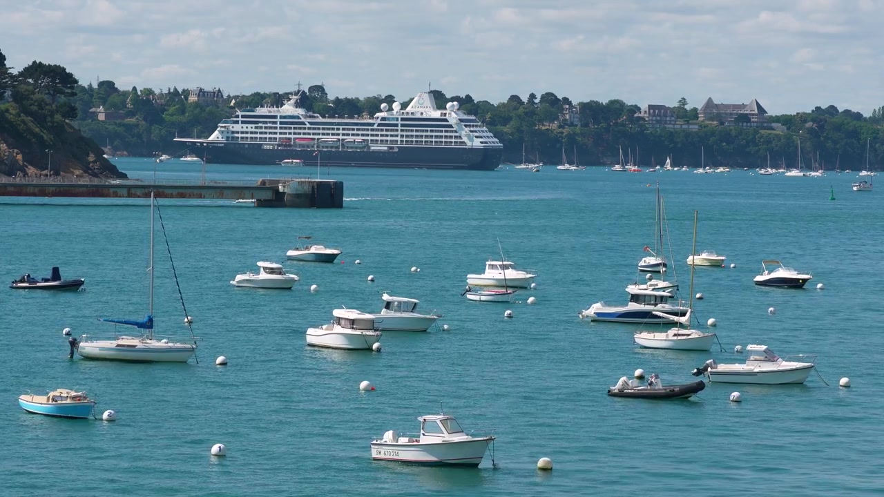 Filmisk udsigt over små både, der ligger for anker i havnen med et krydstogtskib i baggrunden, filmet i Saint-Malo, Bretagne, Frankrig.
