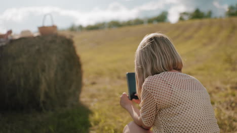 rear view of lady squatting taking photos of her sister in vast farmland with blurred background, warm countryside scene with hay bale and golden sunlight