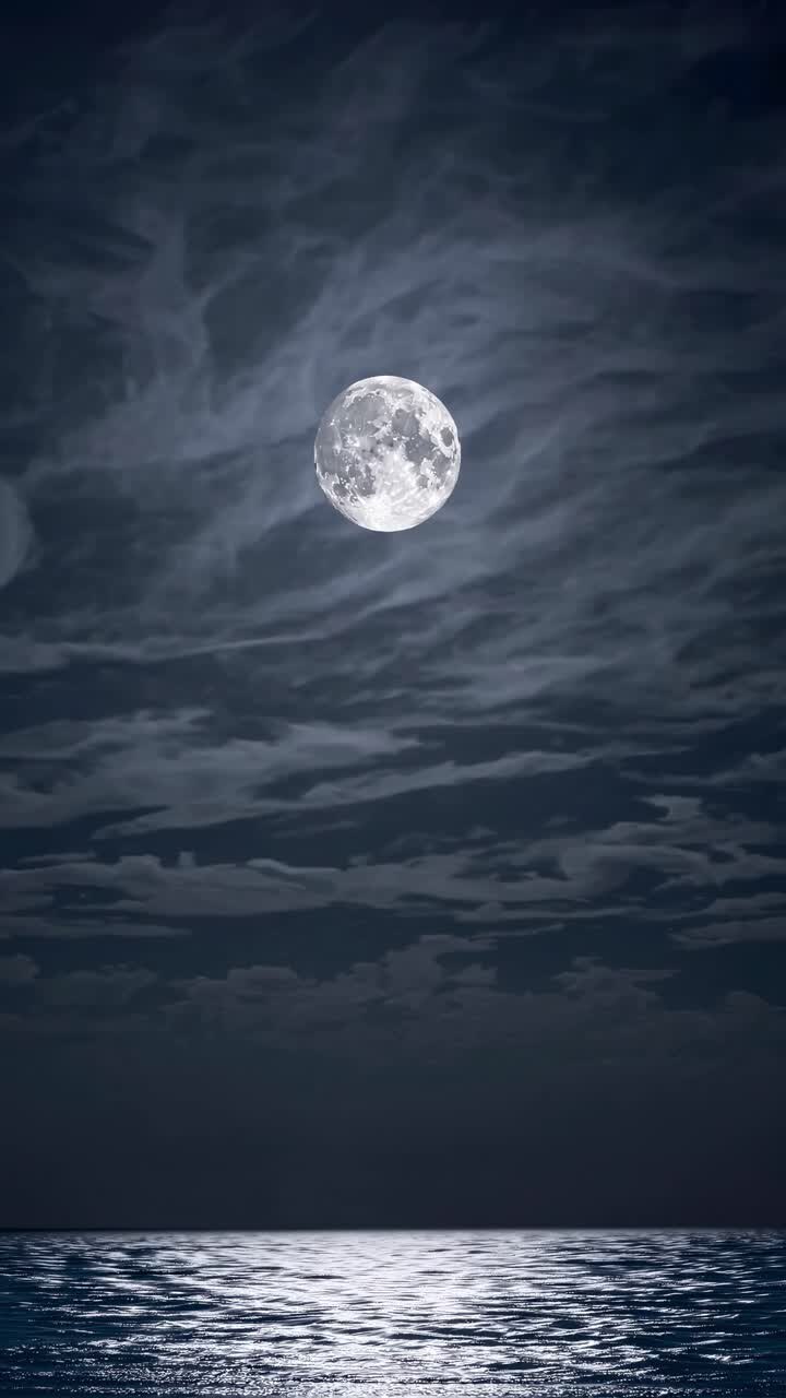 Uma cena noturna serena com uma lua cheia iluminando o oceano. Capturada de um ângulo baixo