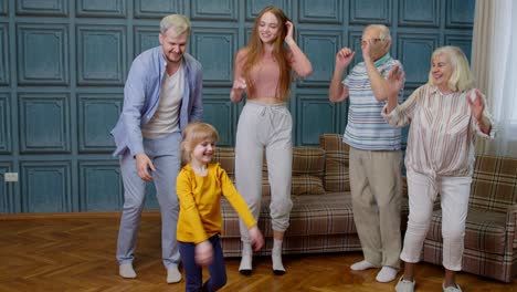 family members of different generations having fun listening music, dancing crazy in room at home