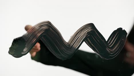 close-up of a hand painting a black wavy line with a brush
