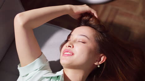 a young woman is combing her hair using her fingers while lying doing on a couch to relax.
