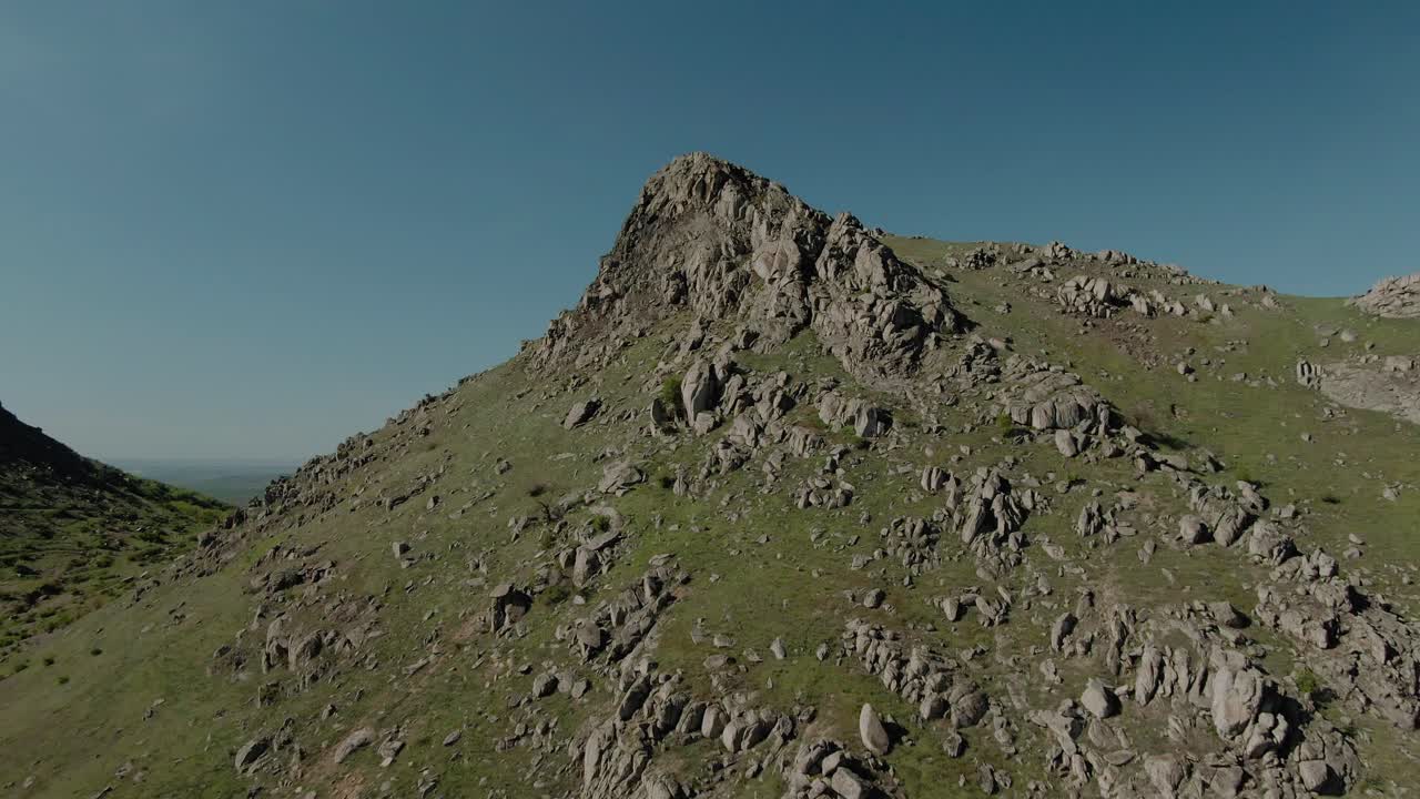 Aerial shot flying towards an old eroded mountain peak on a sunny clear day