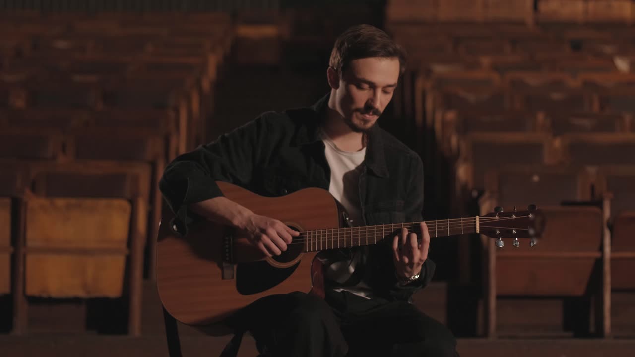 Un chico apuesto toca una guitarra acústica en un cine abandonado. El músico canta una canción y se acompaña con la guitarra