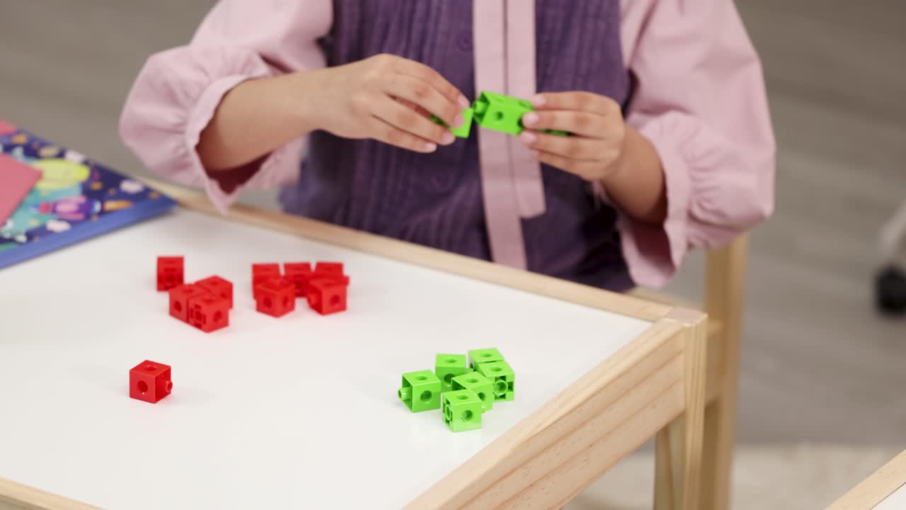 A child sorts red and green plastic blocks on a white table in a classroom