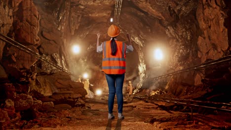 full body back view of a female engineer with safety helmet raising her hands celebrating while working in underground mine tunnel