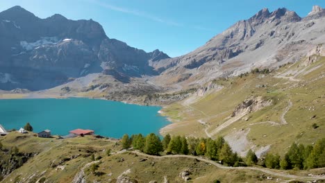 Aerial-flyover-over-the-shores-of-Lac-de-Salanfe-in-Valais,-Switzerland-on-a-sunny-autumn-day-in-the-Swiss-Alps-with-a-view-of-an-alpine-landscape,-mountain-peaks,-cliffs-and-hydroelectric-dam