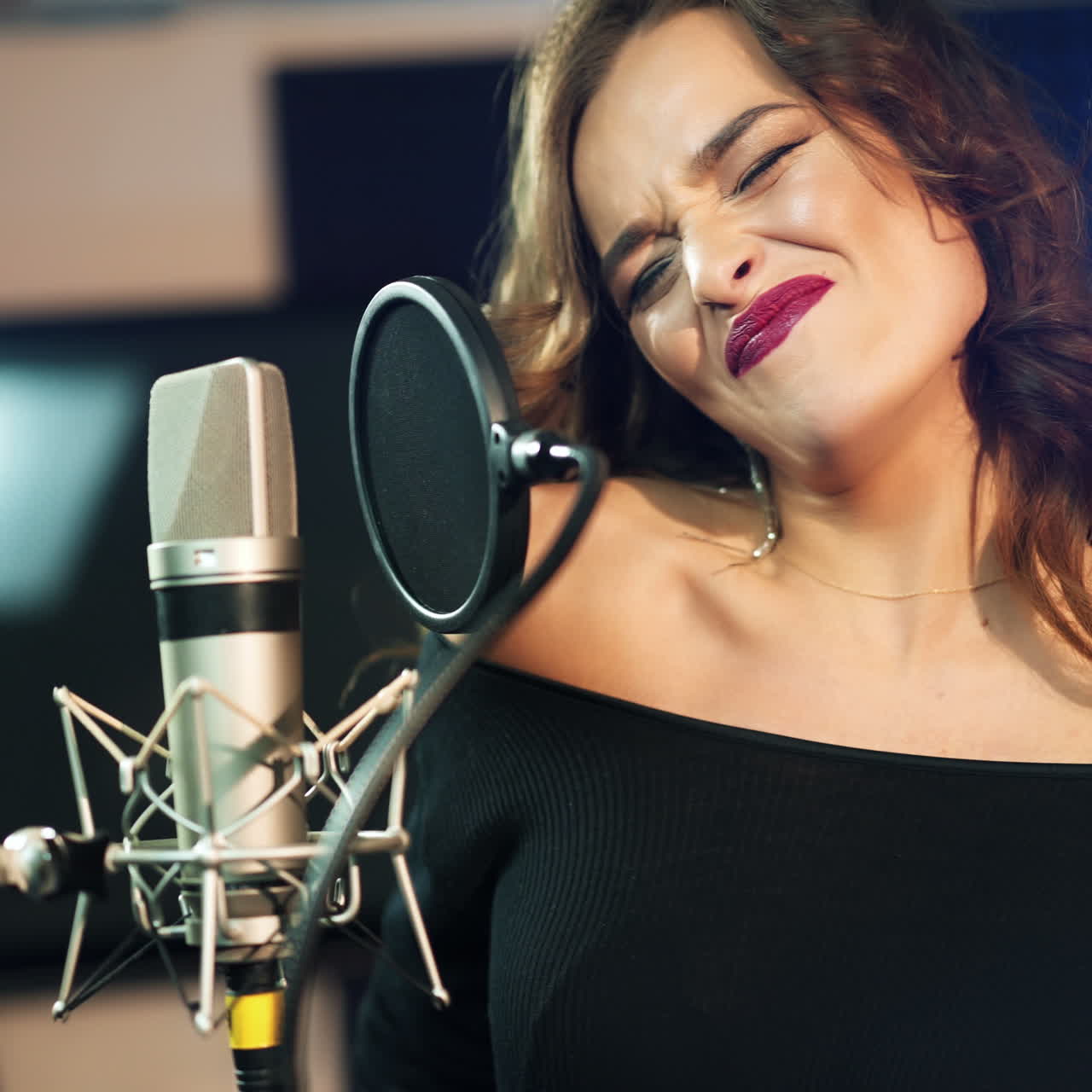 Young brunette woman recording a song or album in a professional studio. Beautiful girl singing emotionally near the modern microphone in sound room.