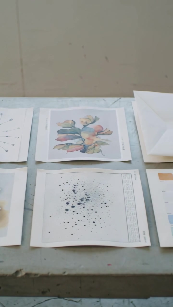 Vertical video: Panning camera moving across art table to show prints, swatch chart, folded sheets
