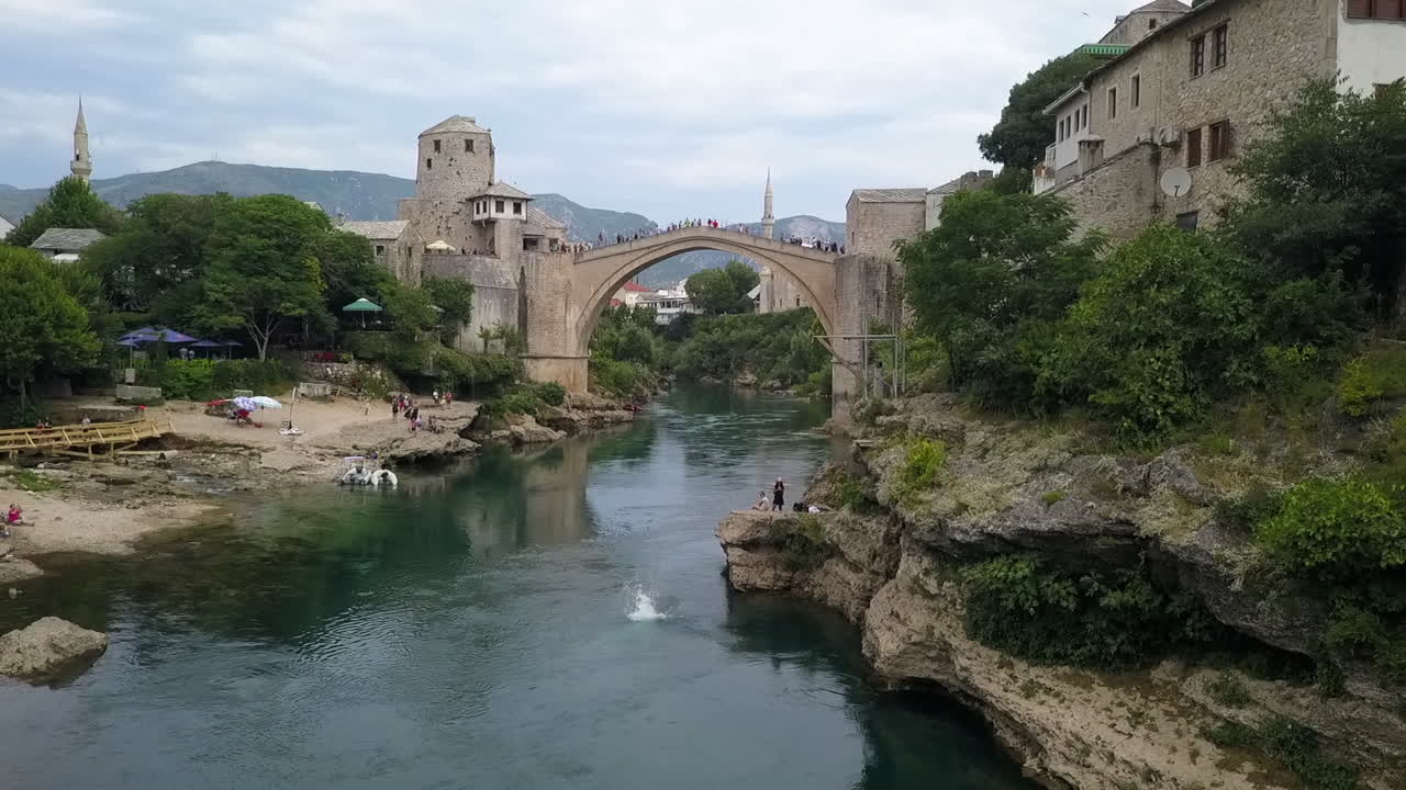 남자는 mostar old bridge 보스니아 근처의 높은 플랫폼에서 공중제비 다이빙을 합니다.