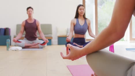 caucasian female instructor, diverse man and woman sitting in lotus position on mats at yoga class