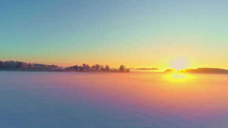 aerial drone shot over frozen lake during cold winter foggy sunrise with silhouette of trees visible in the background