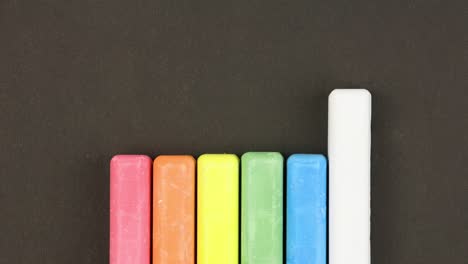 six colored children crayons on black background lined in row, first crayons come out sequentially then randomly, close-up, loop video, stopmotion animation, kindergarten education concept