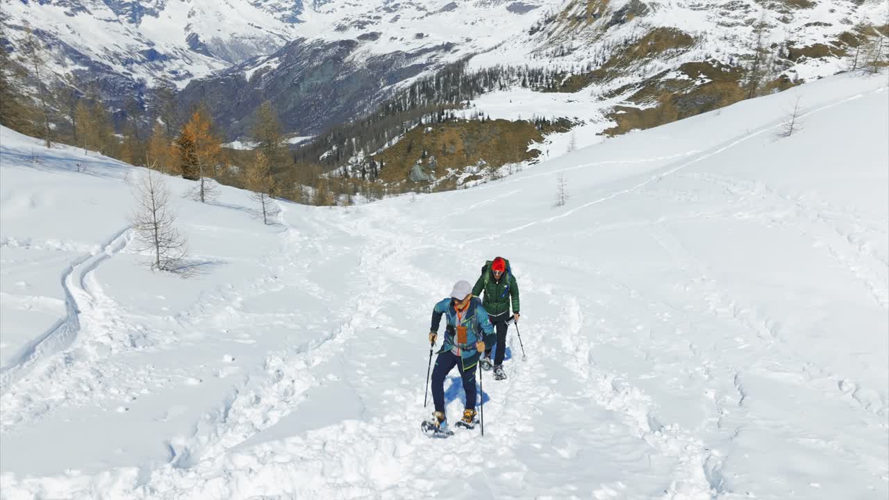 Couple of snowshoers walking snowy trail, winter sports, Italian Alps. Aerial drone low altitude
