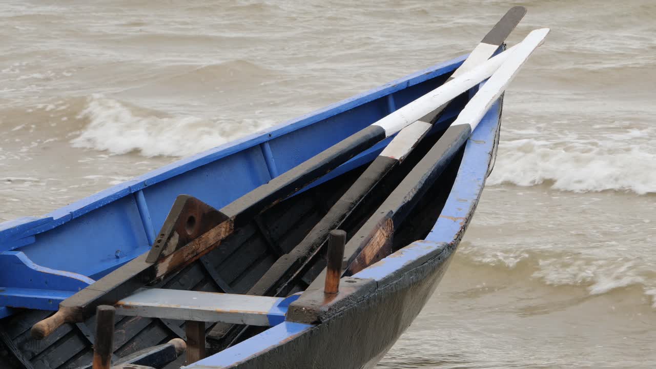 Stævn af en currach-båd og traditionelle træårer stablet foran, mens bølgerne slår ind