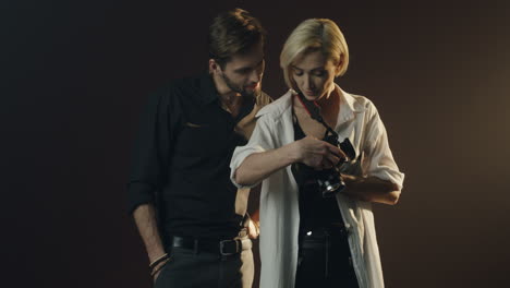 young male model and female photographer showing photos after photoshoot on the camera screen in dark studio