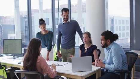 grupo diverso de colegas creativos masculinos y femeninos reunidos en una mesa con una computadora portátil en discusión