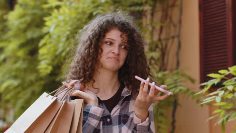 Woman shopaholic consumer after shopping sale with full bags with gifts outdoors talking on phone