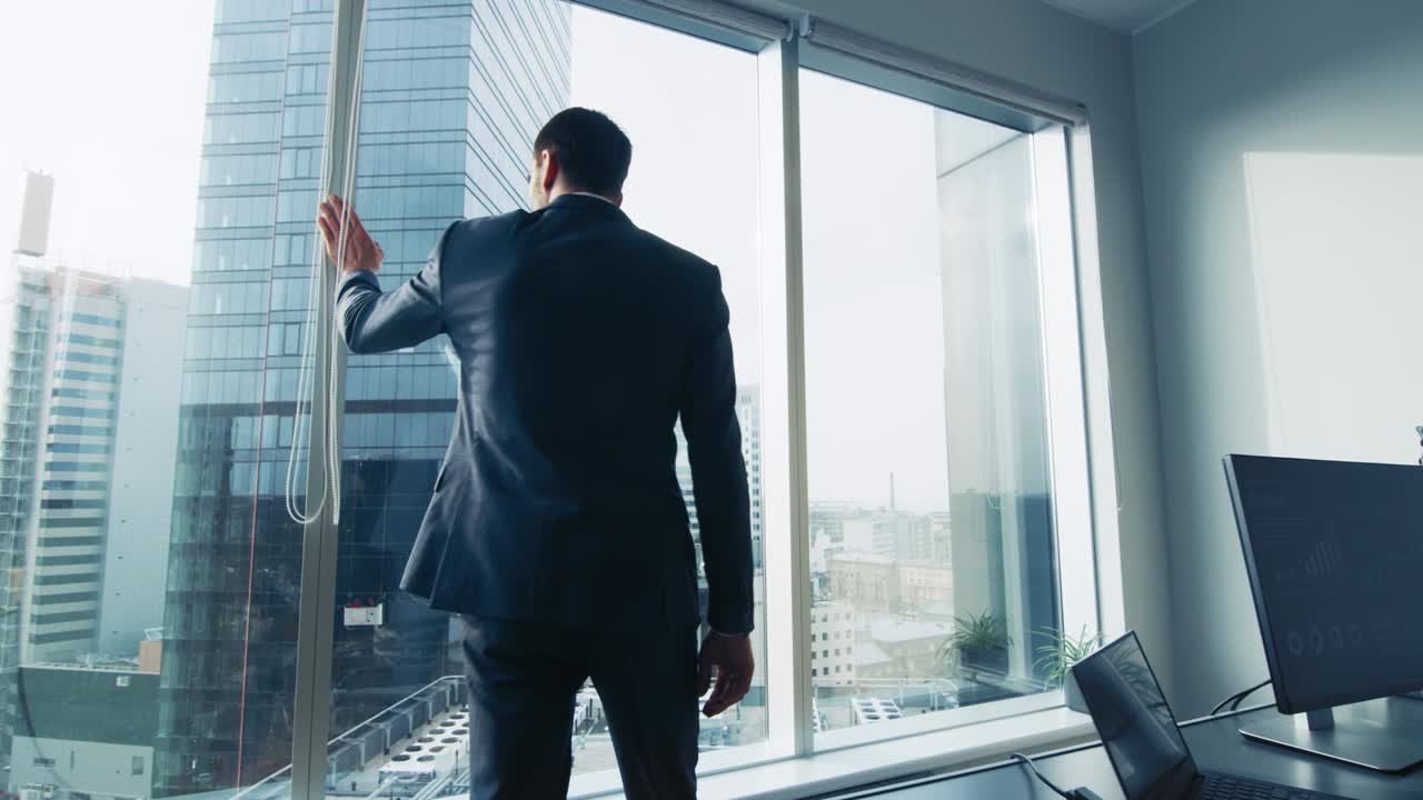 hombre de negocios pensativo con traje de pie en su oficina, mirando por la ventana y contemplando el próximo gran contrato de negocios. distrito de negocios de la ciudad principal con vista panorámica de la ventana. colores azules.
