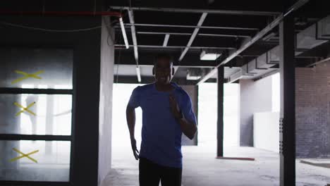 African american man wearing sports clothing jogging through an empty urban building