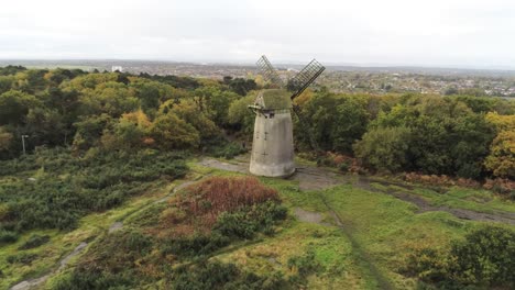 Traditional-wooden-stone-flour-mill-windmill-preserved-in-Autumn-woodland-aerial-view-countryside-fast-push-in