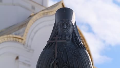 estatua de bronce de un sacerdote frente a una iglesia