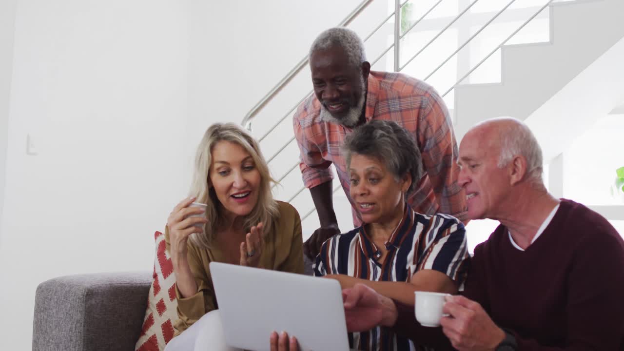Two diverse senior couples sitting on a couch using a laptop and laughing