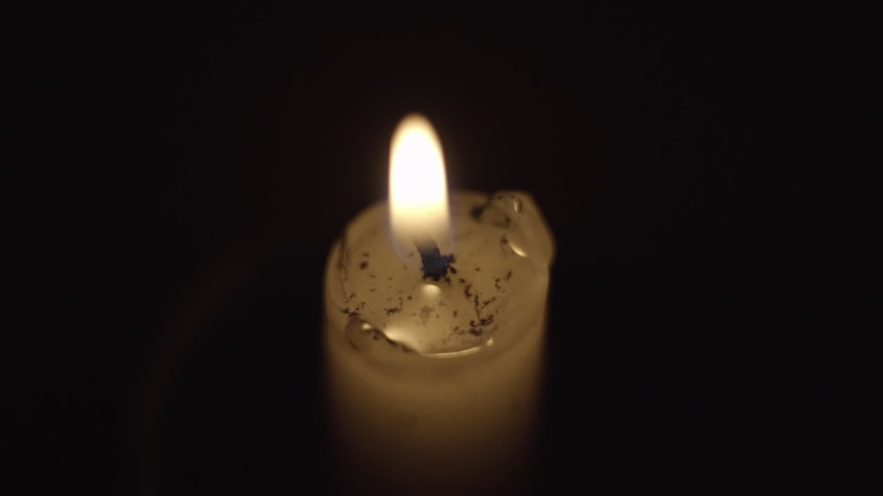 Macro di una fiamma di candela mentre piccoli frammenti di cenere galleggiano nella cera fusa.