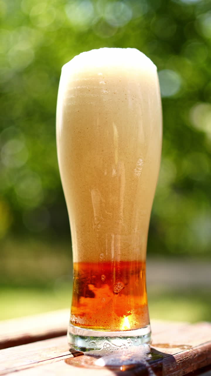 Full glass of white foam from beer. Process of becoming beer beverage from foam in the glass on blurred background. Bubbles and foam in beer glass. Vertical video