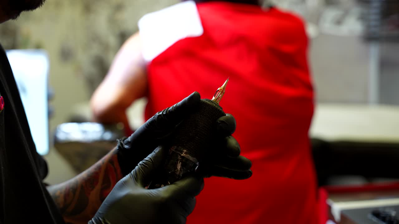 Close up shot of a tattoo artist regulating the pen used for tattooing the ink with a client waiting
