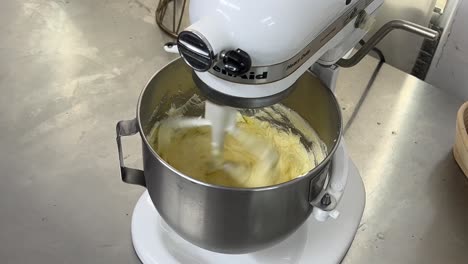 tilt down shot of heavy duty kitchen appliance electric mixer with cake batter cake mixtures mixing smoothly and evenly in the stainless steel bowl