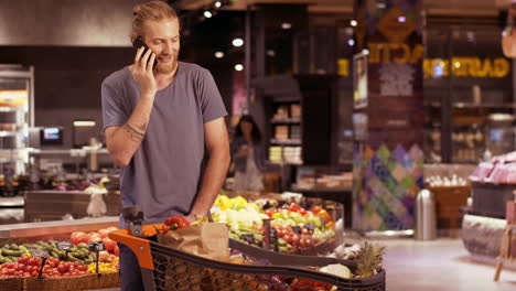 caucasian young man checking products while talking and laughing on smartphone in a supermarket