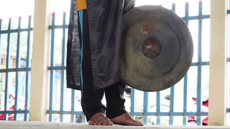 unrecognizable buddhist monk hit steel gong as call for prayer in temple