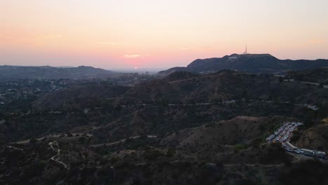 Aerial-drone-view-of-a-busy-road-and-the-sunset-above-the-Hollywood-hills-in-LA