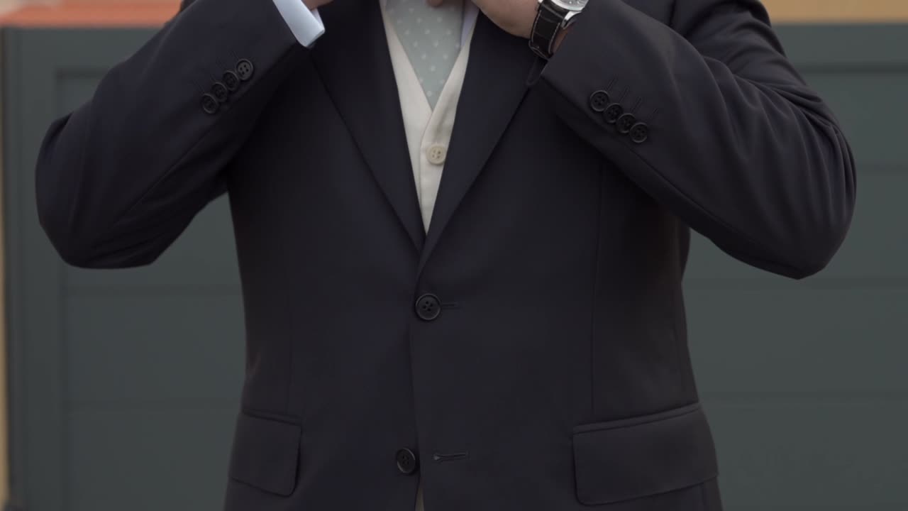 groom in a black suit with a luxury watch adjusting his jacket