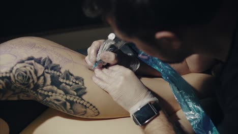artista del tatuaje trabajando en un tatuaje en el muslo