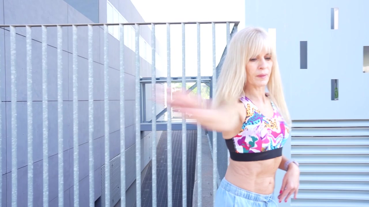 Una donna vivace in un abbigliamento sportivo colorato che passeggia accanto all'esterno di un edificio moderno.
