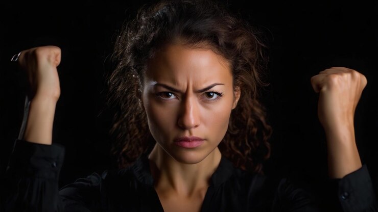 Intensa espressione facciale di determinazione e forza dimostrata da una donna con capelli ricci e pugni alzati, su uno sfondo scuro in un'inquadratura ravvicinata