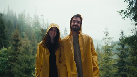 pareja feliz: un chico y una chica con chaquetas amarillas de pie contra el telón de fondo de un bosque de montaña brumoso y sonreír