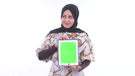 portrait of beautiful muslim woman smiling and thinking while showing digital tablet with copy space against white background