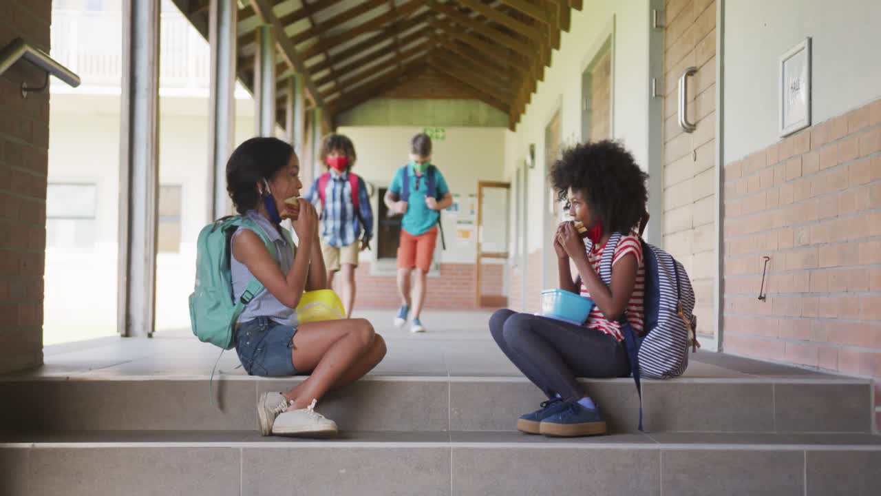 학교에서 계단에 앉아 있는 두 소녀가 티핀 박스에서 점심을 먹고 있다.