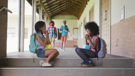 Two-girls-eating-lunch-from-tiffin-box-while-sitting-on-stairs-at-school