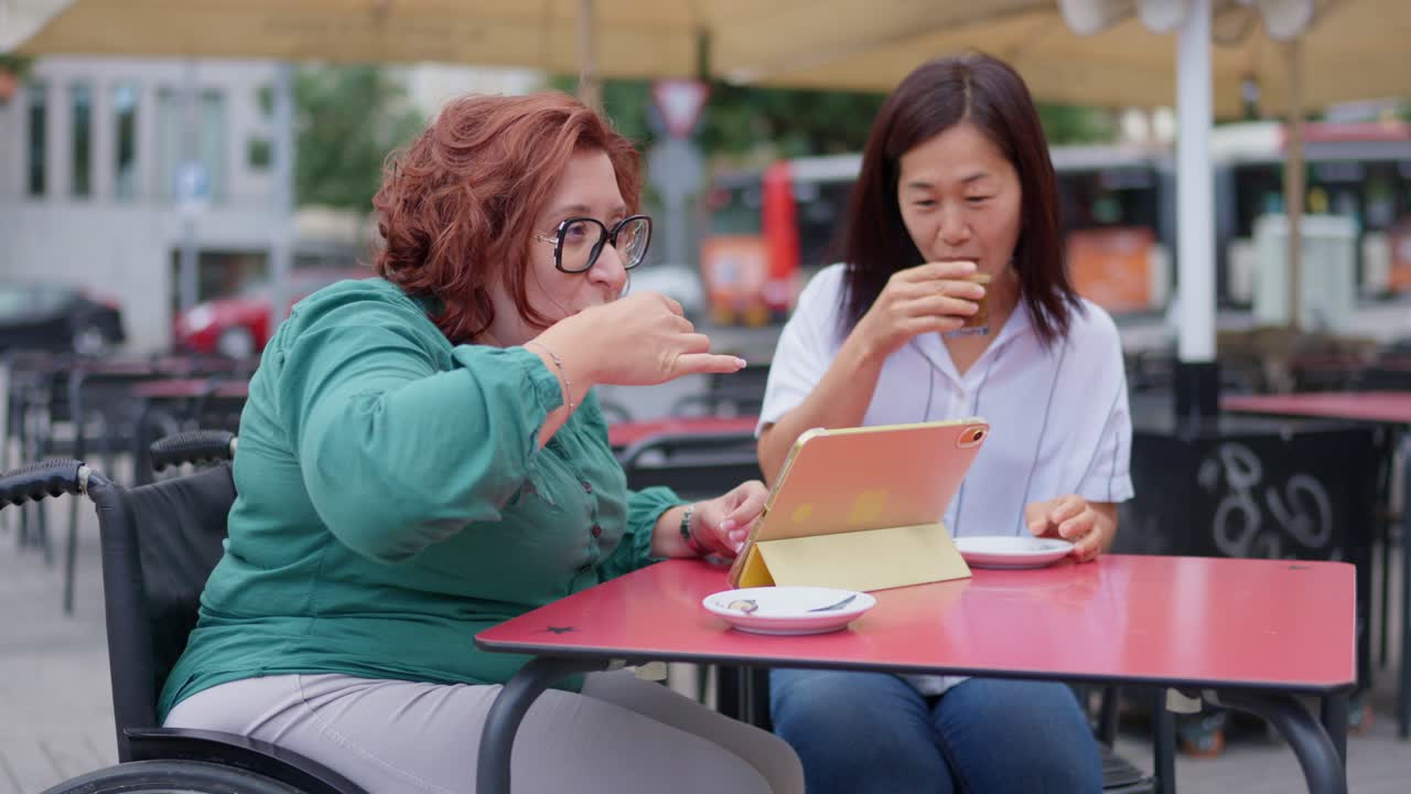 Two women at an outdoor cafe with a tablet