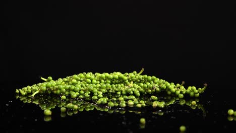 green peppercorns fall and bounce on a reflective black surface, captured in slow motion with dramatic lighting